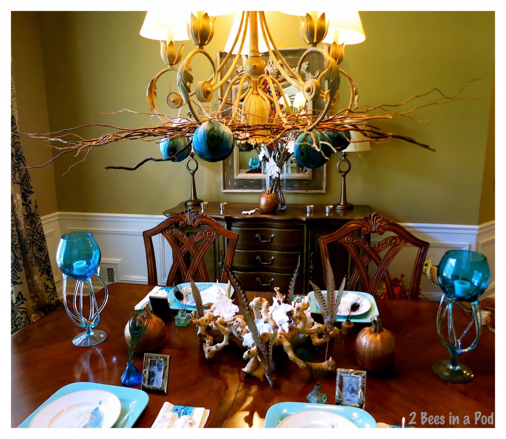 Curly willow branches and round peacock ornaments adorn the chandelier above the turquoise and copper Fall tablescape.